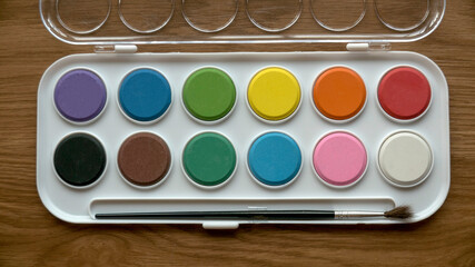 Top view of colorful watercolor palette with brush on wooden background.