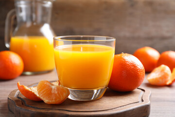 Glass of fresh tangerine juice and fruits on wooden board