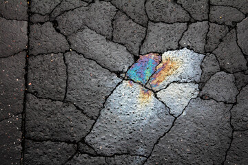 Artistic, abstract high contrast picture, with rainbow colors oil spill on cracked dark concrete on...
