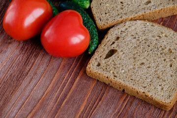 Two heart-shaped tomatoes lie on a wooden table along with bread and gherkins. Flat lay. Close up. Copy space