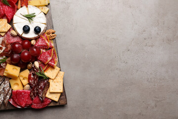 Wooden board with different appetizers on grey table, top view. Space for text