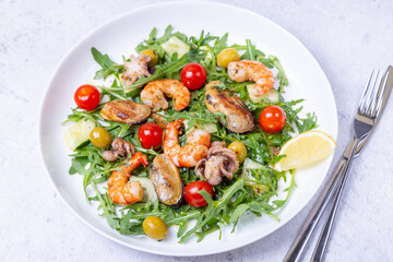 Fototapeta na wymiar Salad with seafood, arugula, tomatoes, cucumbers and olives on a white plate. Close-up.