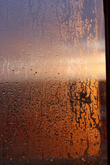Vertical natural background with water drops on a window with sun rays, condensation on glass with dripping drops