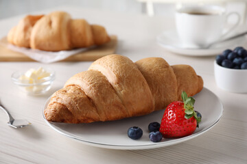 Plate with fresh crispy croissant and berries on white wooden table