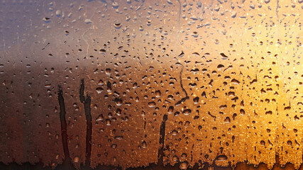 Horizontal natural background with water drops on the window with sunbeams, condensation on the glass with dripping drops