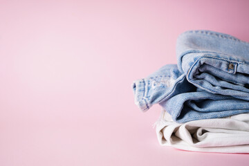 Folded assorted jeans on a pink background, space fot text.