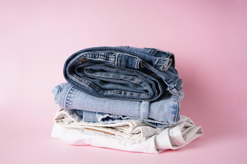 Folded different jeans on a pink background.