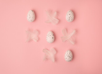 creative layout for easter. quail eggs and white feathers lie randomly on a pink background