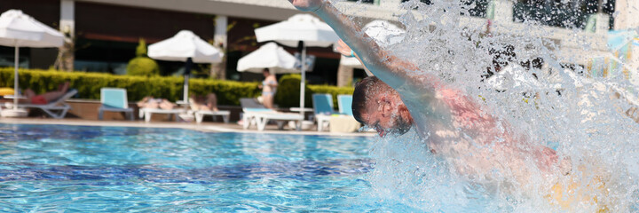 Man swim with breast stroke in blue pool of clear water. Splashes of water fly to sides.