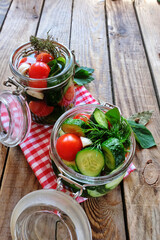 Pickled cucumbers and tomatoes in two glass jars with dill on a brown wooden table. Home preservation, fermentation.. Vegetarina,  organic food, ready for winter. Vertical, copy space.