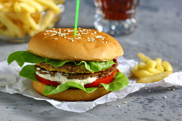 Grilled hamburger with fries and cola on grey background.   Horizontally.
