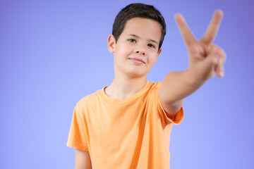 Portrait of little boy showing victory hand sign on purple background