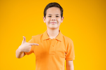 Choose Me. Positive boy pointing at himself and copy space on his blank orange t-shirt for text or promotional content