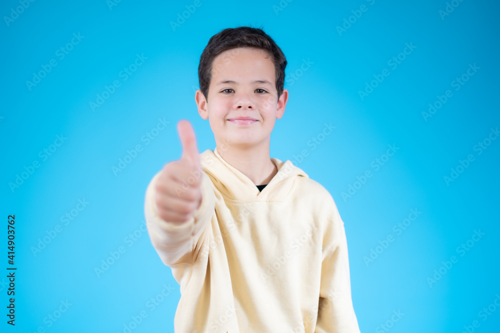 Wall mural cheerful smiling little boy standing over blue background and showing thumbs up