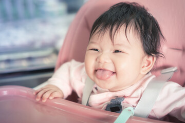 Asian happy baby smiling and sitting on a chair in living room. Cute 6 months baby waiting to eating food at the table.