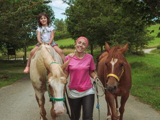 mujer con dos caballos y preciosa niña montando en uno de ellos