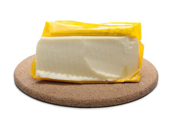 Cow cheese block sliced in half with yellow wrap on cork mat isolated on white background