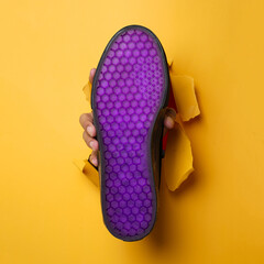 Plain black sneakers with a purple base. Plimsoll shoes on a yellow background give a bright effect to the photo. Front shot. Side shot. Hands holding sneakers through yellow paper background.