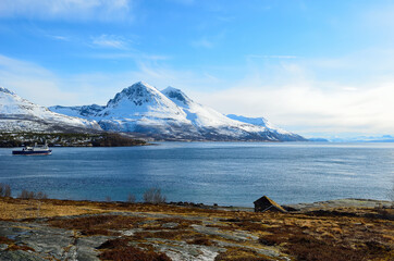 Majestic snow covered mountain with a blue sky and ocean in front in Hella, Norway in spring time