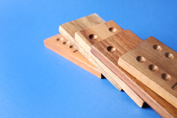 Fallen wooden domino tiles on blue background, closeup. Space for text
