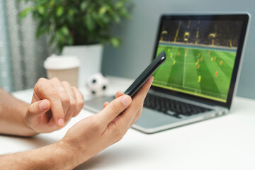 Man watching soccer play live broadcast online on his laptop and making bets on his favourite team using mobile application