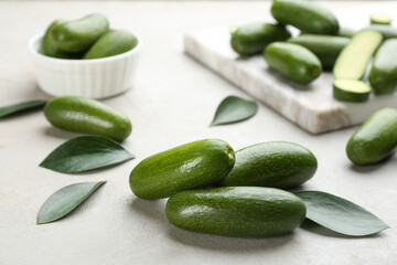 Whole seedless avocados with green leaves on light grey table