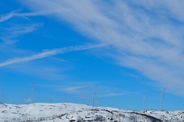 Fototapeta na wymiar windmill farm on snowy mountain in northern Norway in bright sunshine and blue sky backdrop