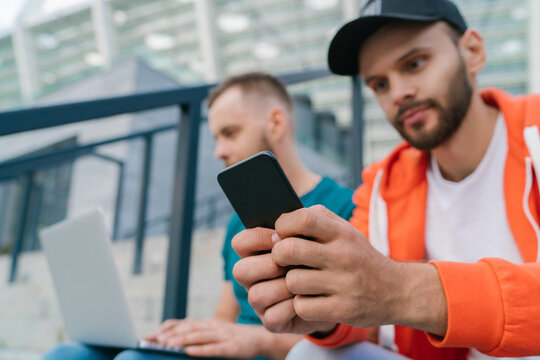 Two friends sitting on football stadium steps and making bets using smartphone and laptop