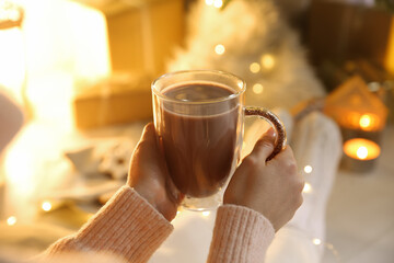 Woman with cup of drink and blurred Christmas lights on background, closeup