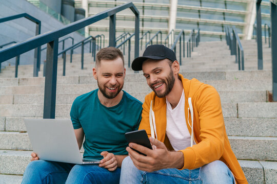 Two friends sitting on football stadium steps and using online betting service on their laptop
