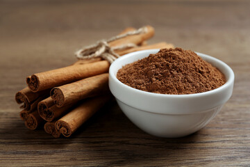Cinnamon powder and sticks on wooden table, closeup