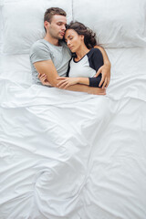 Fototapeta na wymiar Above view of young romantic couple hugging in bed while sleeping