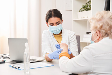 Fototapeta premium Doctor examining elderly patient while measuring her pulse