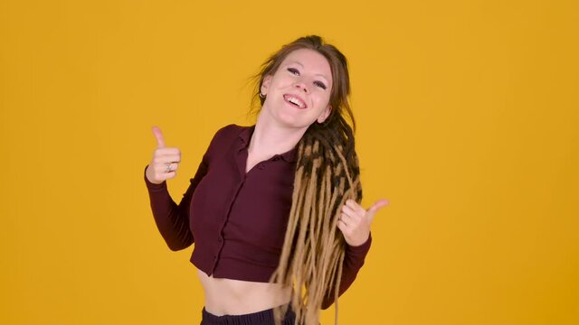 Happy young girl with dreadlocks posing isolated on yellow background. People emotions lifestyle concept. Girl tenager doing winner gesture