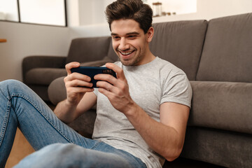 Happy brunette guy playing video game on mobile phone at home