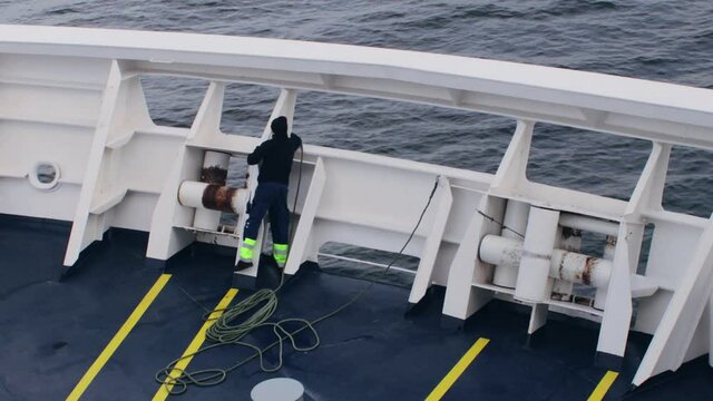 Seaman threads guide rope around edge of ship in preparation to moor