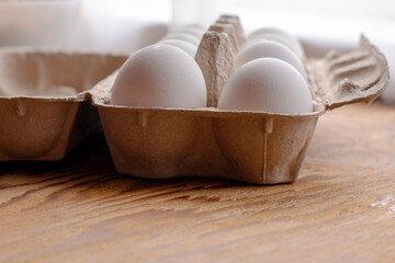 white chicken eggs in a paper tray stand on the table close up