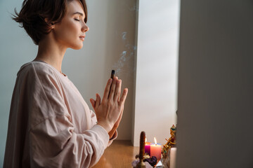 Peaceful girl holding frankincense while praying at home shrine