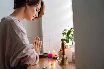 Peaceful beautiful girl praying at home shrine indoors