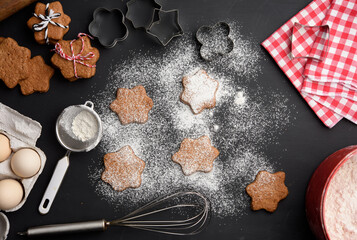 Star shaped baked gingerbread cookies sprinkled with powdered sugar on a black table