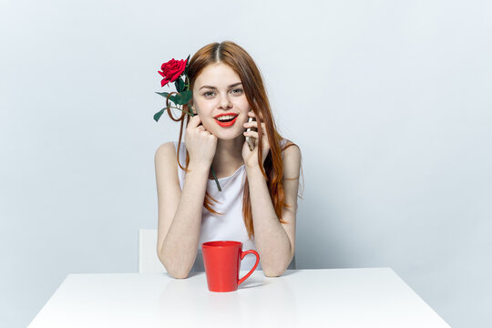 pretty woman sitting at the table with red rose flower and talking on the phone