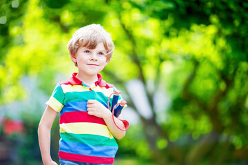 Funny little kid boy shooting wooden slingshot against green tree background. Portrait of happy...