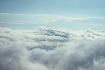 Naklejka na ściany i meble Wonderful minimalist landscape with mountain top above dense low clouds. Mountain vertex floats in thick clouds. Scenic minimalism with mountain peak above cloudy sky. Beautiful summit in cloudiness.