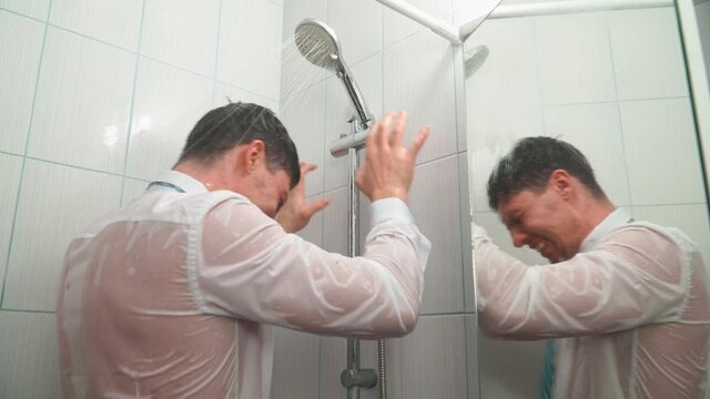 Sad Man in White Shirt and Tie Stands in Bathroom under Shower and Bathes in his Clothes. Evil Disappointed Guy in Office Clothes is Crying from Failure and Misfortune. Depression and Emotional Stress
