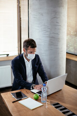 Naklejka premium Businessman with a medical mask working in his office on laptop. Young man working on a new project.
