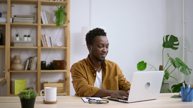African man work at laptop in home office. Spbas male entrepreneur typing text on computer keyboard. Relaxed employee does job distantly online. Concept guy, casual