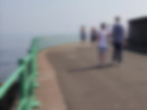Abstract blurred adult couple walk along a seaside promenade in the sunshine