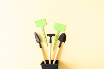 Miniature gardening tools and inscription board in flowerpot on beige background.
