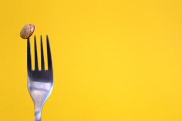 Pistachio nut strung on a fork on a yellow background