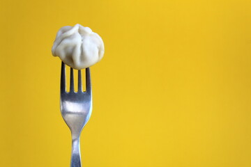 Delicious meat one dumpling impaled on a fork on a yellow background